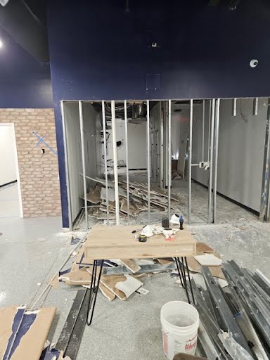 Commercial construction site with metal studs, hanging electrical wiring, and debris clearing in a large open space.